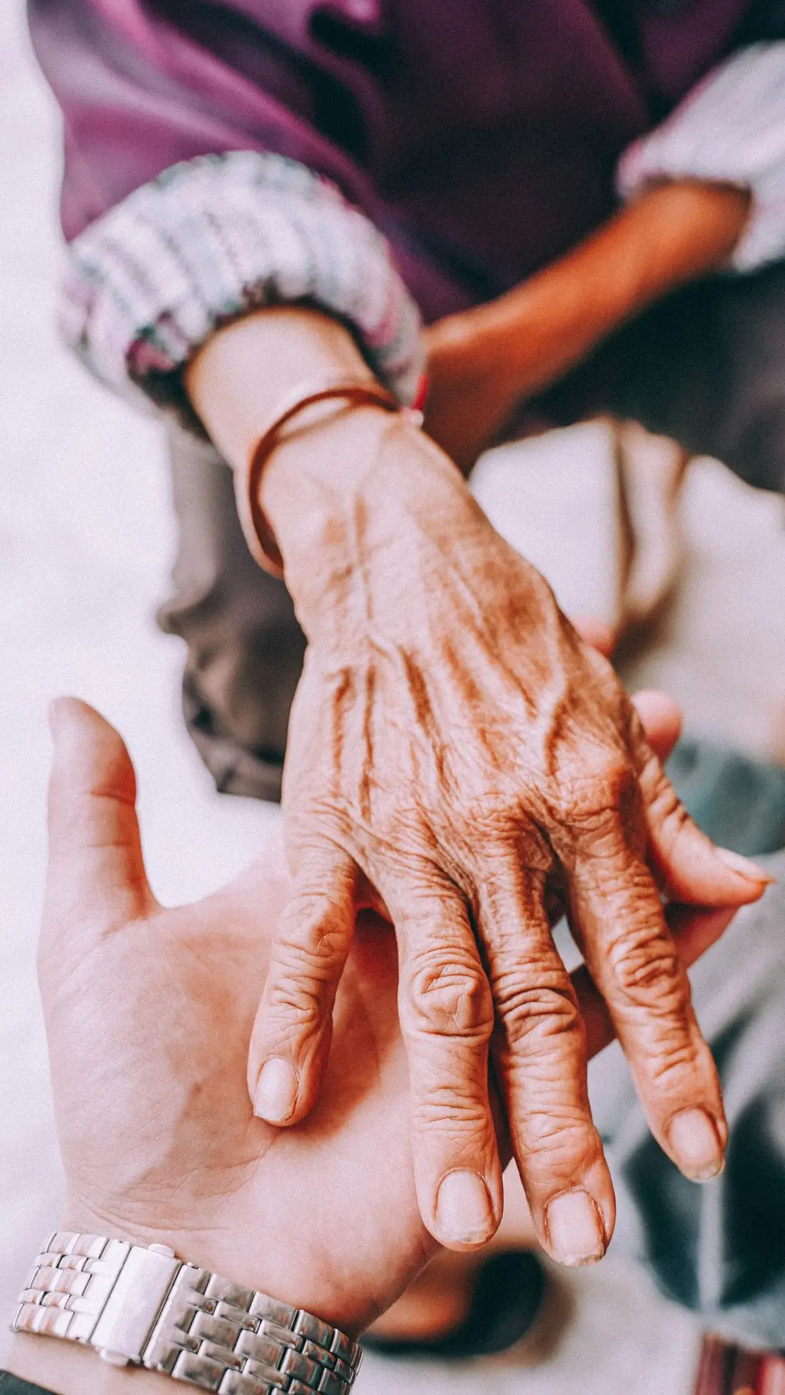 A younger hand gently cradling an older adult's hand